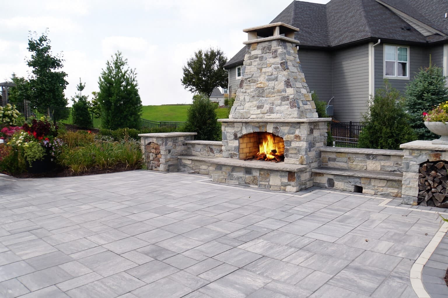 Finished paver patio with a stone fireplace and firewood storage